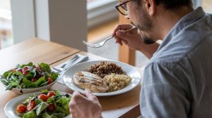 Hombre disfrutando de una comida saludable, con pollo y ensalada, demostrando que se puede comer con carillas dentales alimentos blandos y nutritivos.